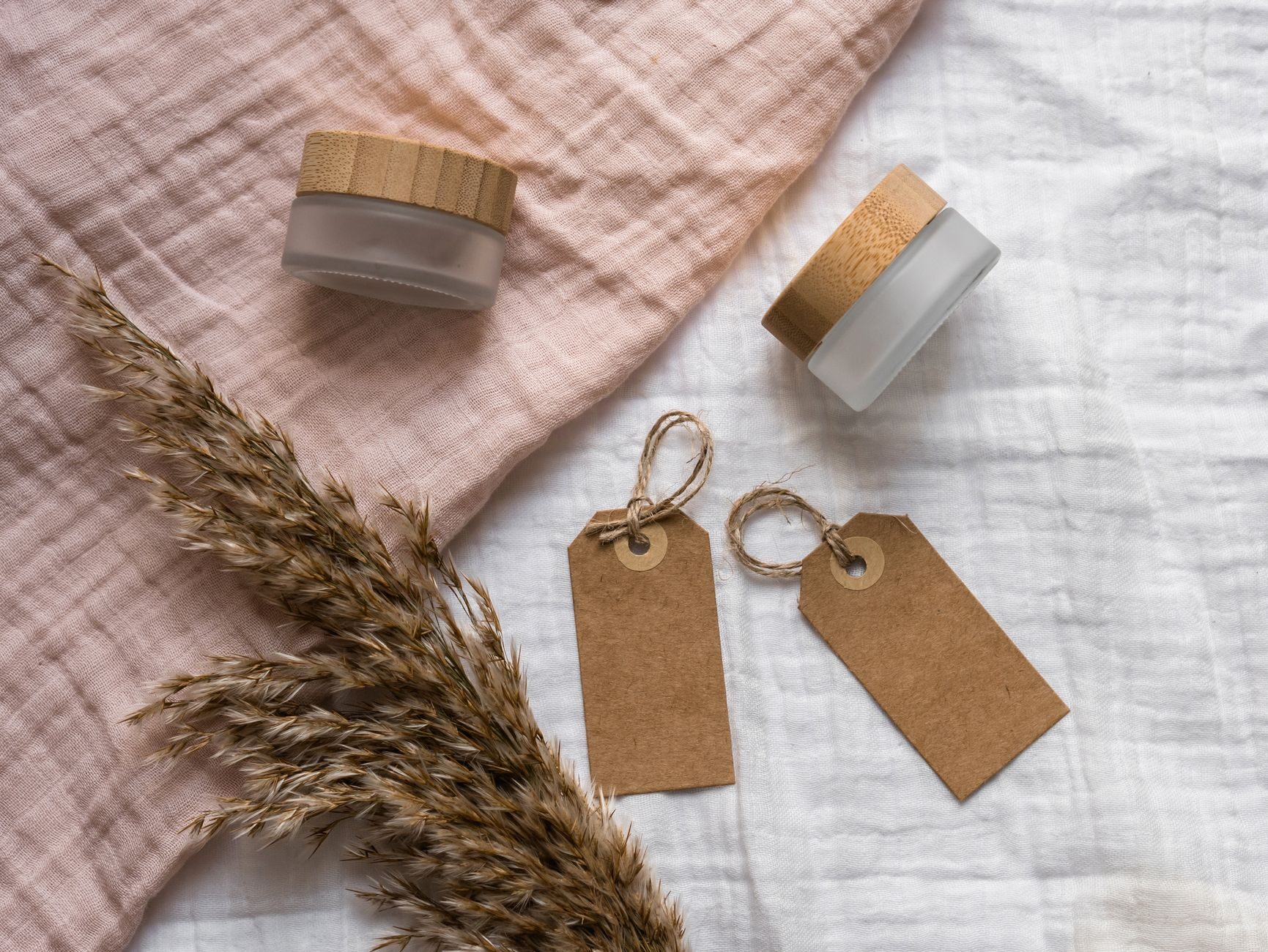 Two frosted glass jars with kraft gift tags on blush linen with pampas grass