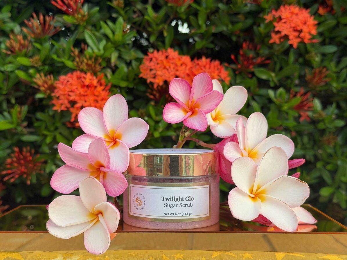 Twilight Glo lavender sugar scrub jar with plumeria against green foliage