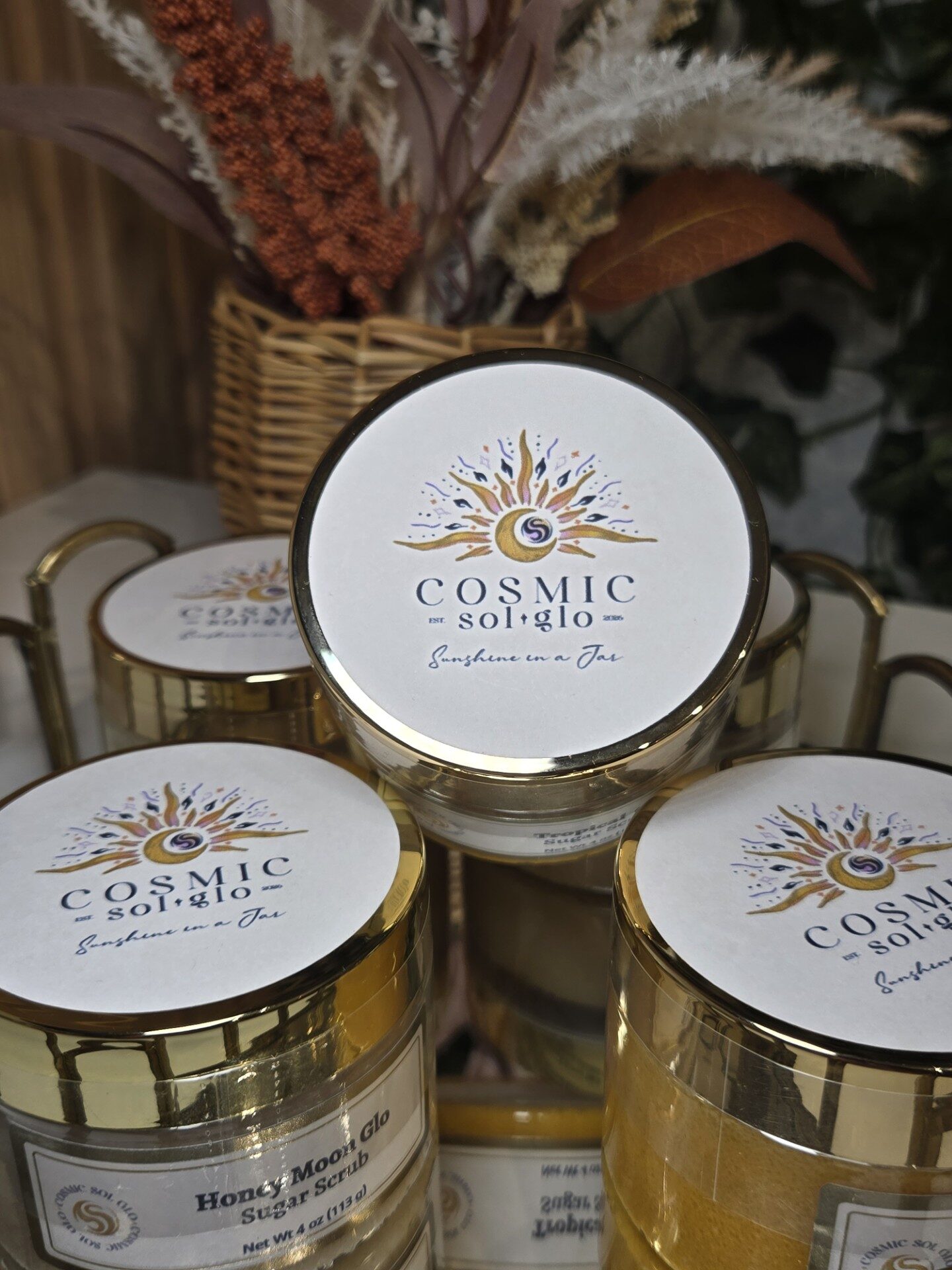 Top-down cluster of Cosmic Sol Glo branded lids with dried pampas grass and a rattan basket
